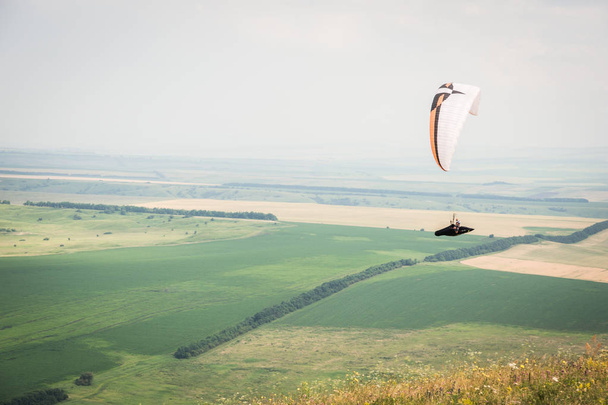 White orange paraglide with a paraglider in a cocoon against the background of fields of the sky and clouds. Paragliding Sports - 写真・画像