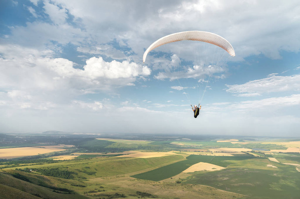 White orange paraglide with a paraglider in a cocoon against the background of fields of the sky and clouds. Paragliding Sports - Фото, изображение