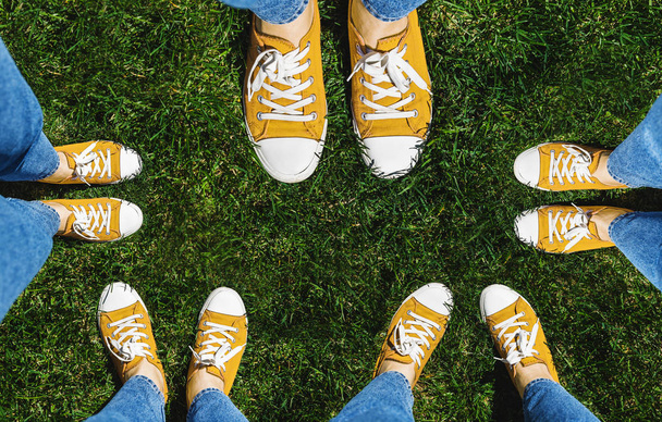 Collage de piernas en viejas zapatillas amarillas sobre hierba verde. Vista desde arriba. El concepto de juventud, primavera y libertad. Aislado sobre fondo blanco
. - Foto, imagen