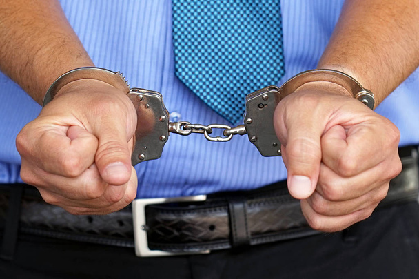 Arrested man handcuffed hands. Businessman in office in handcuffs holding a bribe. Arrested man in handcuffs. Prisoner or arrested terrorist, close-up of hands in handcuffs. Selective focus. Hacker. - Photo, Image