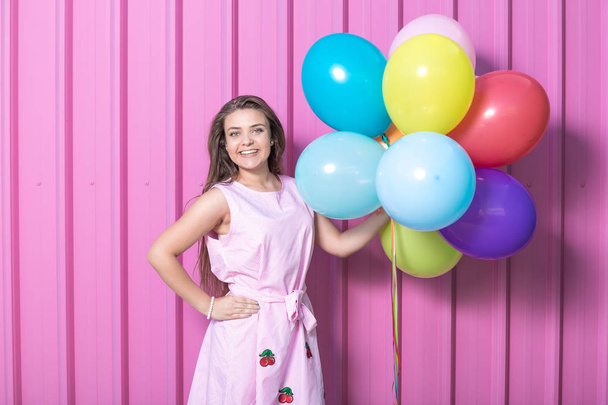 Beautiful young woman holding colorful balloons on pastel pink background. - Valokuva, kuva