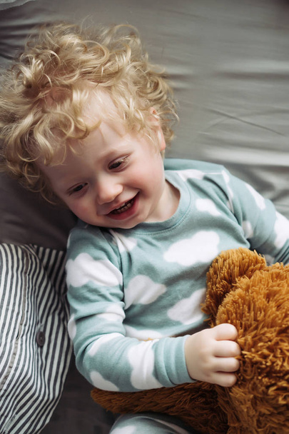 small fair-haired baby boy in cute blue pajamas laughs, holds his stuffed toy - Foto, imagen