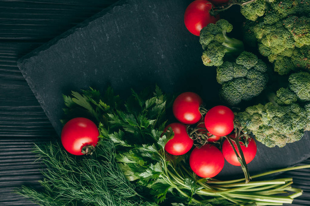 On a dark wooden table, fresh green broccoli, parsley, dill and cherry tomatoes for your health. Recipe. Ingredients. Dietary food. Place under the text. Top view - Foto, Imagem