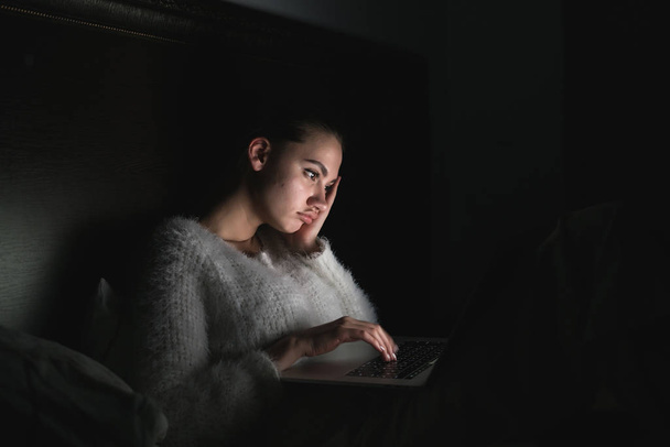 tired young girl sitting in bed late at night in the dark watching a boring movie on her laptop - Фото, зображення