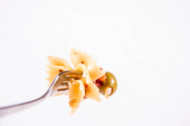 Farfalle pasta with sun dried tomato, ham and olives on a fork on a white background - Zdjęcie, obraz