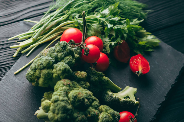 On a dark wooden table, fresh green broccoli, parsley, dill and cherry tomatoes for your health. Recipe. Ingredients. Dietary food. Place under the text. Top view - Photo, image