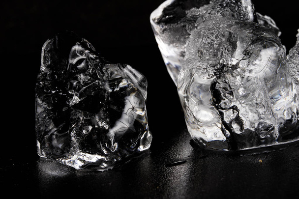 Ice on a black table. Melting piece of frozen water in a warm room. Black background. - Foto, afbeelding