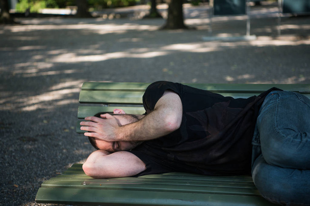 Chudák bezdomovci spící na dřevěné lavičce v parku - Fotografie, Obrázek