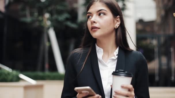 Professional young businesswoman walking on urban street using smartphone and drink coffee. Concept: new business, communication, banker. Outside, slow motion - 映像、動画