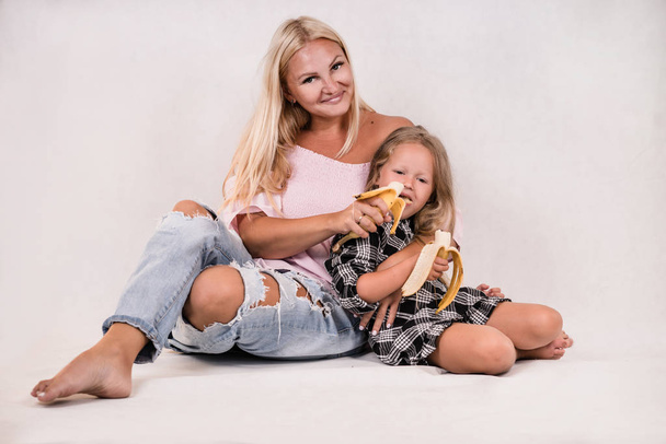 bonito close-knit família mãe e filha sentar e comer banana no fundo branco
 - Foto, Imagem
