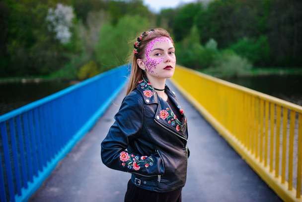 Молодая красивая женщина с фиолетовым блеском на лице стоит на мосту
. - Фото, изображение