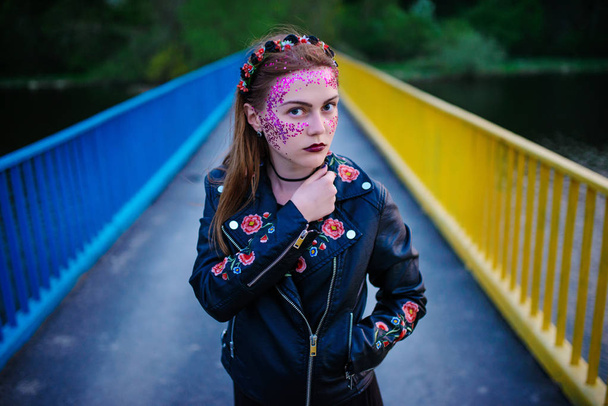Μια νεαρή όμορφη γυναίκα με βιολετί λάμψη σε πρόσωπο στέκεται στη γέφυρα. - Φωτογραφία, εικόνα