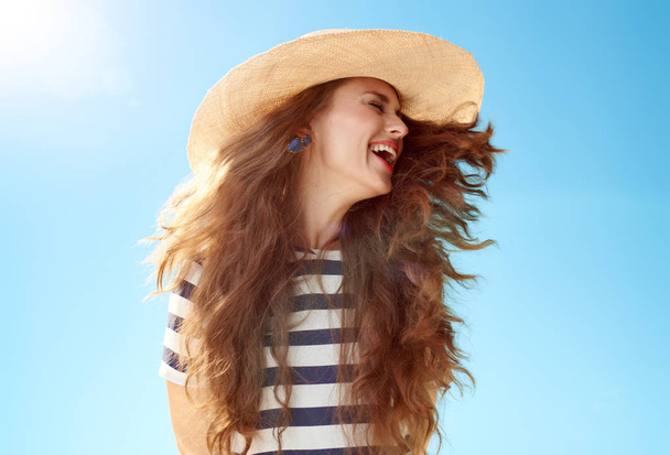 attractive happy woman in straw hat with fluttering hair against blue sky - Photo, Image