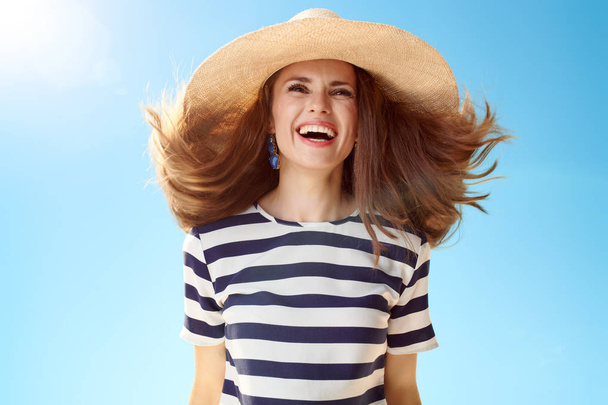 smiling young woman in straw hat with fluttering hair against blue sky - Valokuva, kuva