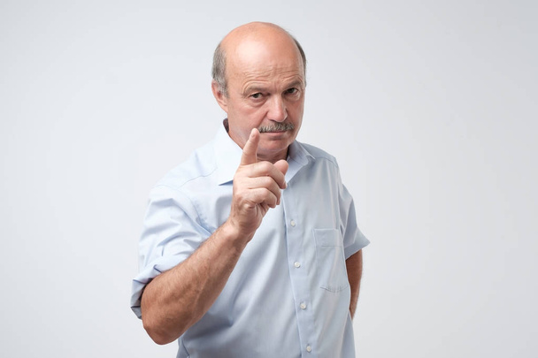 Portrait of serious senior man with warning finger and blue shirt shirt against light gray background. You better listen to my advice concept - 写真・画像