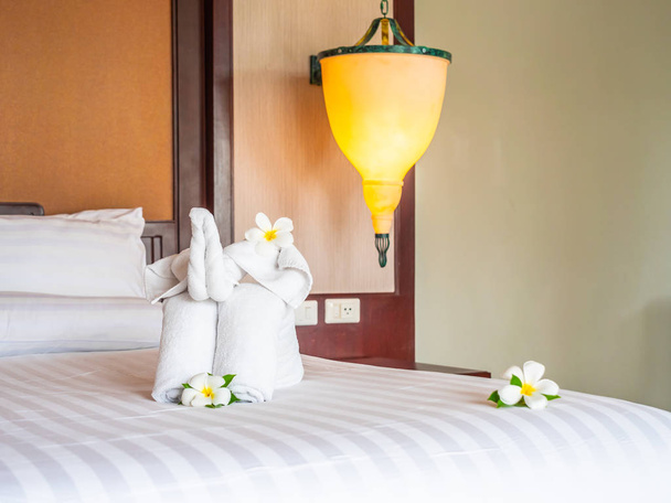 Toalla de elefante blanco y almohada cómoda en la decoración de la cama en el interior del dormitorio del hotel
 - Foto, Imagen