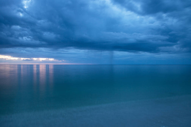 Rain pours from dark clouds over Clam Pass Beach in Naples, Florida around sunset. - Photo, Image