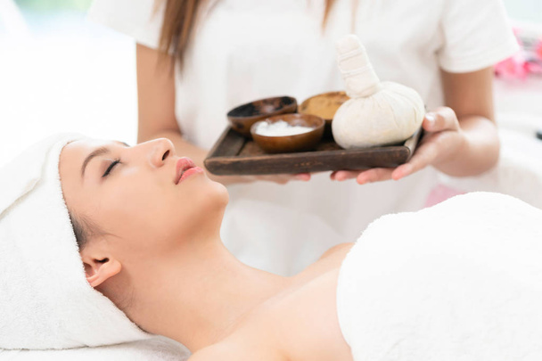 Relaxed woman lying on spa bed prepared for spa massage with therapist holding spa treatment set in background. Luxury wellness, stress relief and rejuvenation concept. - Photo, Image