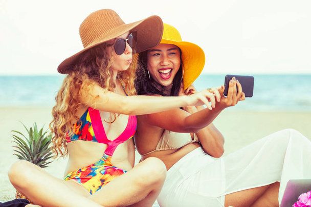 Happy women in bikinis taking selfie photograph from mobile phone together on tropical sand beach in summer vacation. Travel lifestyle. - Photo, Image