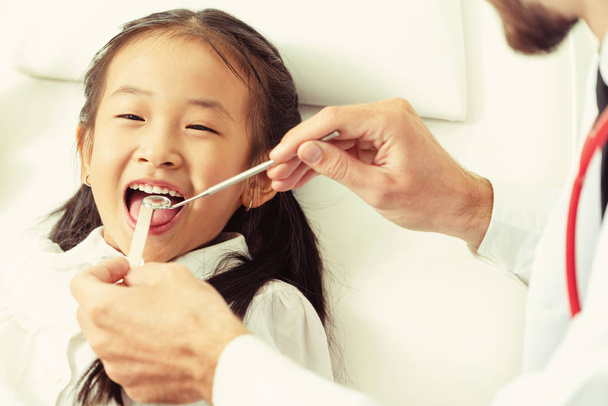 Barátságos fiatal fogorvos vizsgálata boldog gyermek fogak-a fogászati klinikán. Fogászat-koncepció. - Fotó, kép