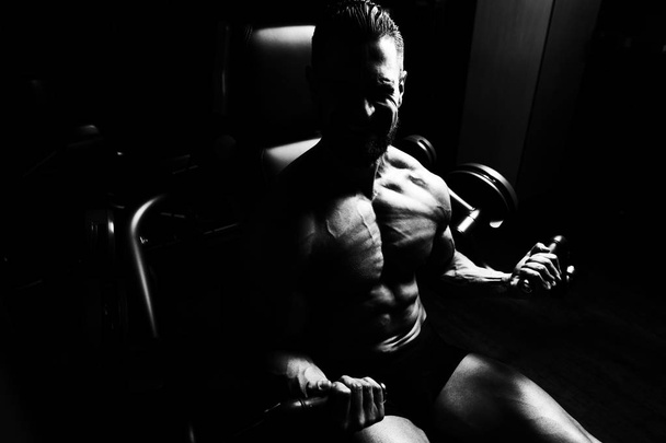 Handsome Muscular Fitness Bodybuilder Doing Heavy Weight Exercise For Biceps On Machine With Cable In The Gym - 写真・画像
