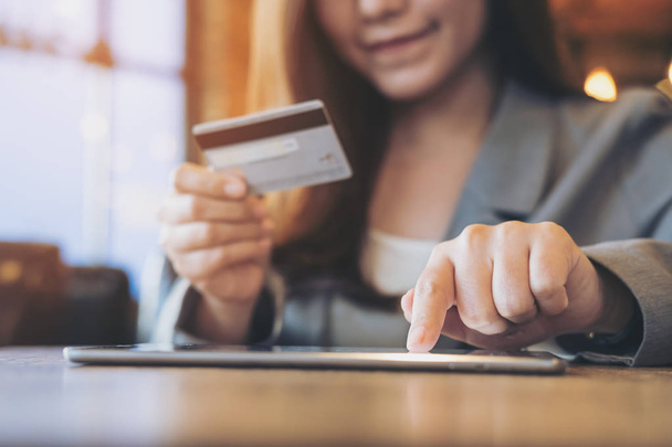eine asiatische Geschäftsfrau mit Kreditkarte, während sie im Coffeeshop ein Tablet benutzt - Foto, Bild
