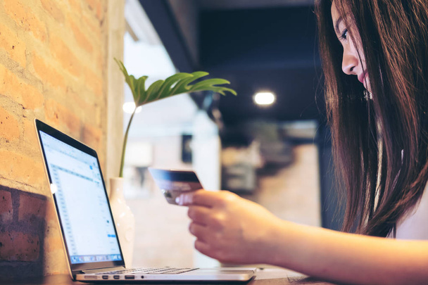 Азиатская бизнес-женщина, держащая кредитную карту во время использования ноутбука в кафе
 - Фото, изображение