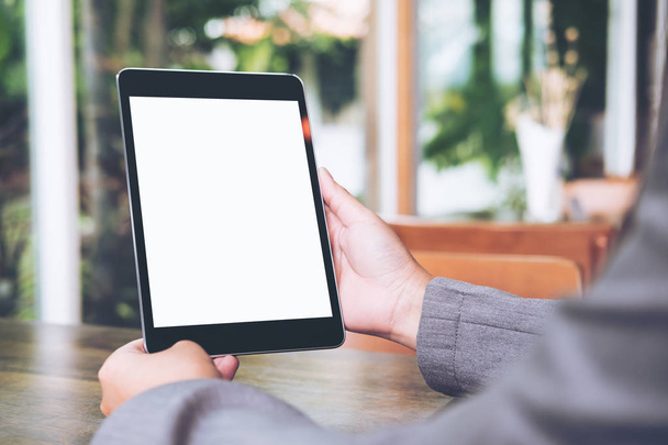 Simular la imagen de las manos de la mujer de negocios sosteniendo la tableta negra con pantalla blanca en blanco en la cafetería con fondo natural
 - Foto, Imagen