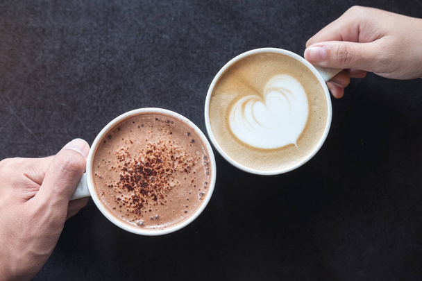 Imagem de vista superior das mãos do homem e da mulher segurando café e copos de chocolate quente com fundo de mesa de madeira
 - Foto, Imagem