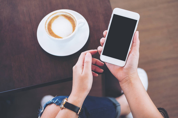 Makieta obrazu biały telefon z puste czarny ekran z filiżanki kawy na drewniany stół i podłogę tle trzymając się za ręce - Zdjęcie, obraz