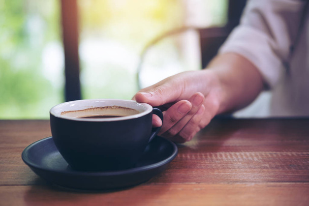 Una mano che tiene una tazza nera di caffè caldo su un tavolo di legno in caffetteria
 - Foto, immagini