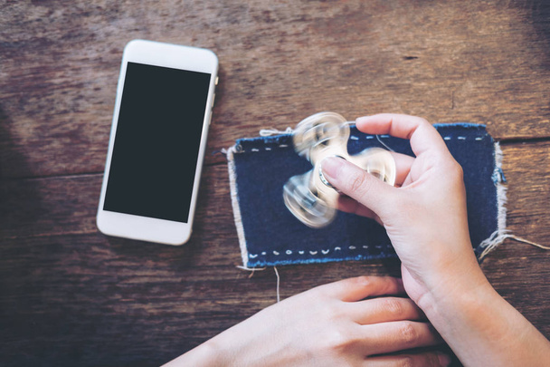 Imagen burlona de teléfono móvil blanco con pantalla en blanco negro y jugando fidget spinner en la mesa de madera vintage en la cafetería
 - Foto, Imagen