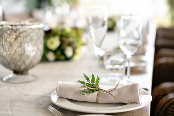 Neatly twisted into a tube dining room napkin decorated with a sprig of pistachio. Wedding Banquet or gala dinner. The chairs and table for guests, served with cutlery and crockery. party on terrace - Foto, afbeelding