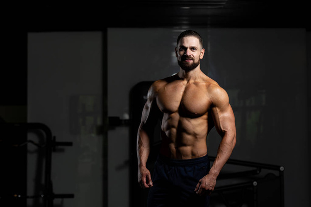 Young Man Standing Strong In The Gym And Flexing Muscles - Muscular Athletic Bodybuilder Fitness Model Posing After Exercises - Φωτογραφία, εικόνα