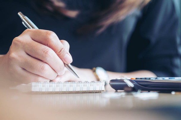 Imagen de cerca de una mujer de negocios trabajando, escribiendo en el cuaderno y utilizando la calculadora en la oficina
 - Foto, Imagen