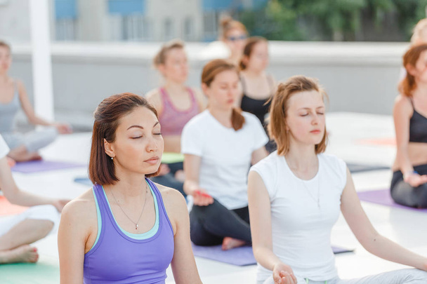 Gruppe fröhlicher, niedlicher junger Frauen, die in Yoga-Asana-Posen sitzen und sich dehnen, Meditation und Trainingskonzept - Foto, Bild