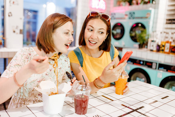 zwei Freundinnen essen Wok-Nudeln in einem Restaurant und schauen auf ein Smartphone - Foto, Bild