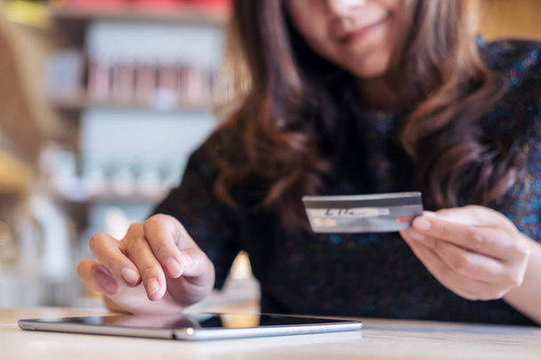Una cara sonriente mujer asiática sosteniendo la tarjeta de crédito y el uso de la tableta PC en el restaurante con sentirse feliz
 - Foto, imagen