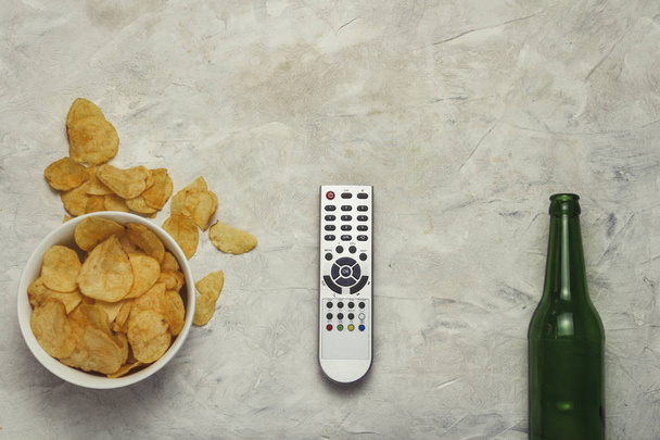 TV remote, a bowl of chips and a bottle of beer on a light background Stone. Flat lay, top view. - Foto, Imagen