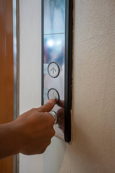 Un dedo pulgar alcanza para presionar el botón del ascensor o ascensor en el edificio de oficinas
. - Foto, imagen