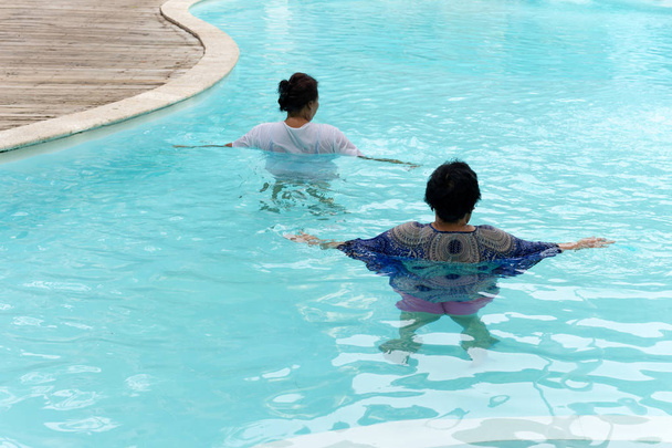 Две пожилые женщины занимаются аквагимнастикой в открытом бассейне
. - Фото, изображение