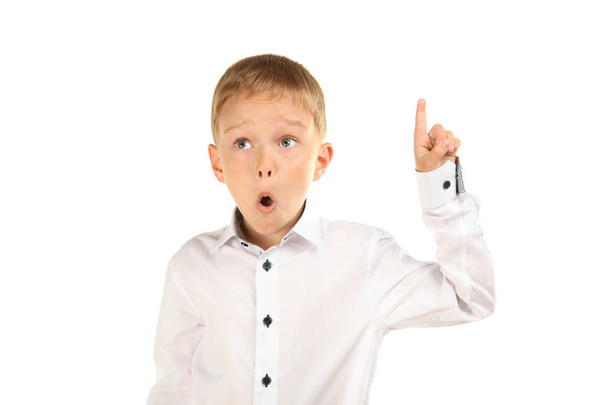 Écolier est surpris de pointer son doigt vers le haut, en chemise blanche, isolé sur blanc. Concept uniforme scolaire
. - Photo, image