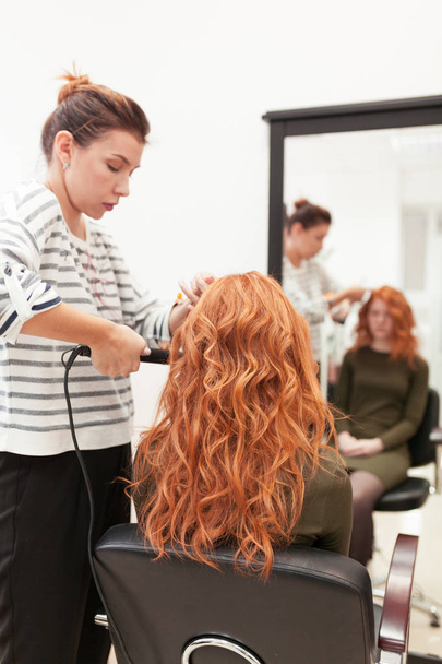 beauty salon, red-haired girl doing make-up and styling in the salon, hairdressers and make-up artist, concept for personal hygiene and beauty - Foto, Imagen