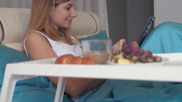 Woman In Bed Uses A Laptop And Near To Her Tray With Breakfast Coffee And Sweets - Video
