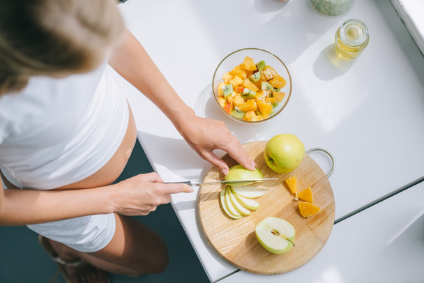 vista aérea de la mujer embarazada con cuchillo cocina frutas ensalada en casa
 - Foto, Imagen