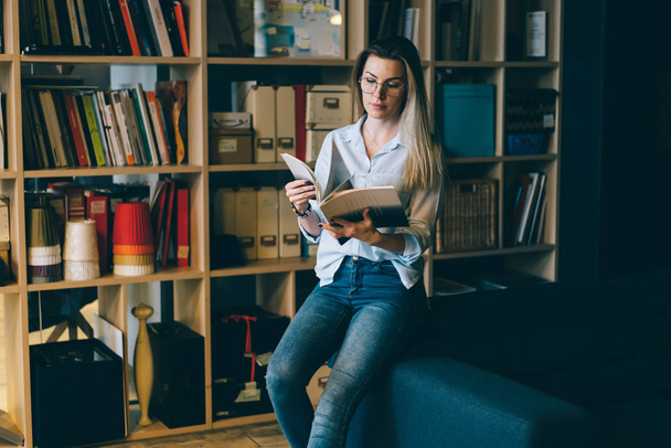 Young attractive talented female student dressed in trendy outfit preparing for upcoming examinations spending time library.Cute hipster girl reviewing information while sitting on comfortable sofa - Fotó, kép