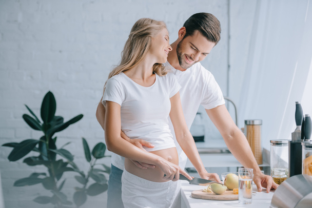 happy pregnant woman and husband cooking fruits salad together in kitchen at home - Valokuva, kuva