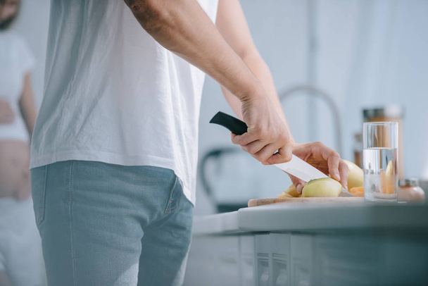 Teilbild eines Mannes, der Obst an der Theke schneidet und schwangere Frau zu Hause in der Küche zurücklässt - Foto, Bild