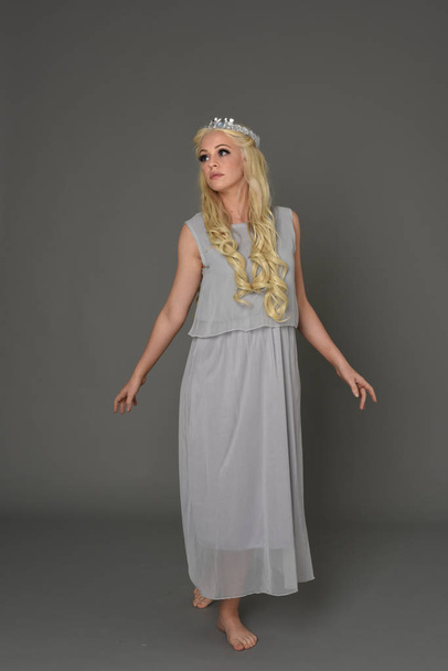 full length portrait of blonde girl wearing crow and grey dress, standing pose.  grey studio background. - Foto, immagini