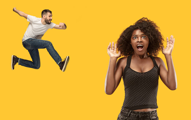 Wow. Beautiful female half-length portrait isolated on gold studio backgroud. Young surprised woman and jumping running man isolated on yellow. Human emotions, facial expression concept. Trendy colors - Photo, Image